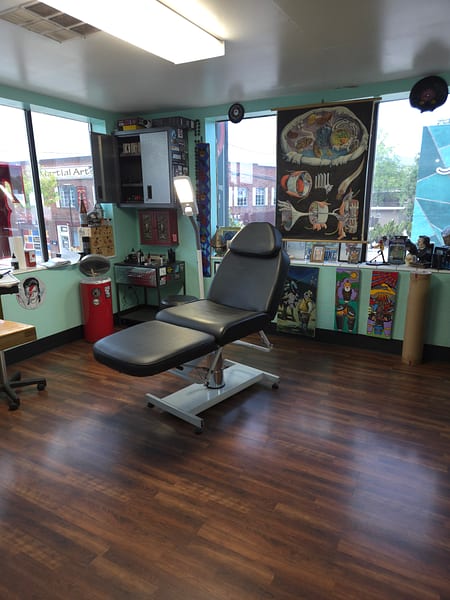 Sunlit tattoo station with a leather chair beside the front windows
