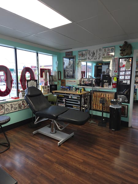 Tattoo station with adjustable chair, teal walls, and framed artwork